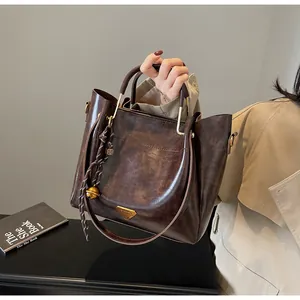 Detail of dark brown tote bag with metallic handles, woven charm and gold hardware