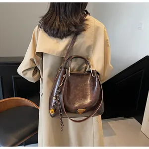 Detail view of a dark brown tote bag with metal logo and charms on a trench coat