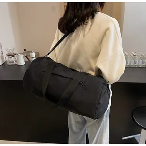 Rear view of a model carrying the large capacity black cylindrical sports gym bag outdoors