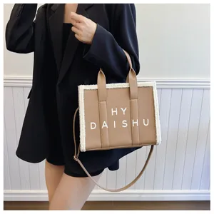 Dettaglio di una borsa tote marrone con bordo in finta pelliccia bianca e scritta HY DAISHU