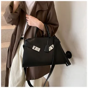 Detailed view of black leather trapezoid tote bag with silver lock and strap on model