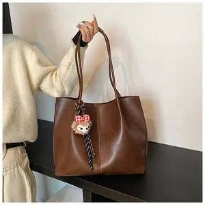 Detail of a brown tote bag with decorative stitching and a plush character pendant
