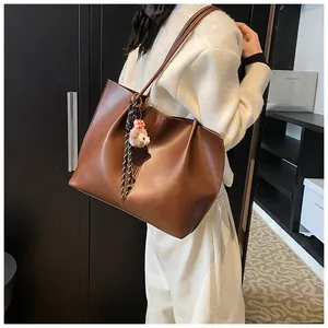 Detail of a large brown faux leather tote bag with a cute sheep plush charm and woven strap