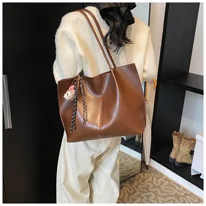 Detail view of large dark brown leather tote bag with a cute decorative charm hanging on side