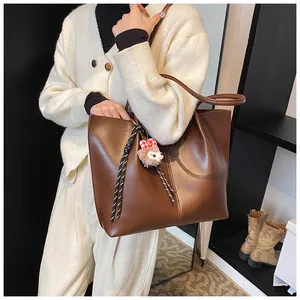 Close-up of brown leather tote bag with decorative vertical stitching and cute puppy pendant