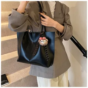 Close-up of black leather tote bag featuring a plush charm on model in grey blazer