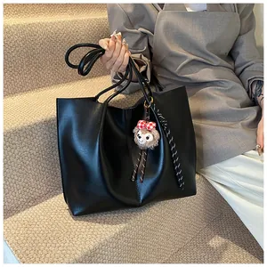Detail view of a large black faux leather tote bag with a plush charm on stairs