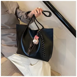Detail of black leather tote bag with a small lamb plush charm and long shoulder straps
