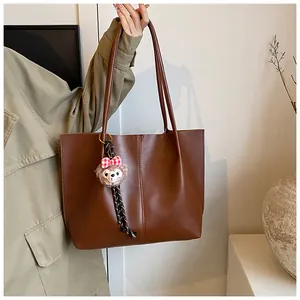 Close-up of deep brown tote bag with central stitching and cute plush doll pendant