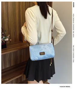 Close-up of light blue denim texture crossbody bag with braided rope strap and gold studs