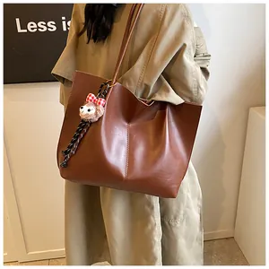 Detail of a brown leather tote bag with a small plush bear charm hanging on the side