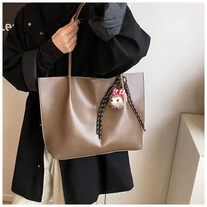 Detail of a brown leather tote bag with a sheep plush charm and woven strap detail