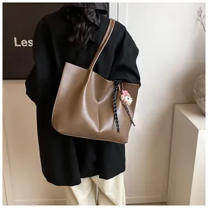 Detailed view of brown matte leather tote with stitching and plush bear charm decoration
