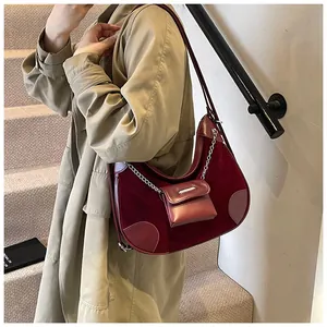 Detalle de bolso de hombro media luna burdeos con acabado de ante y accesorio de mini bolso