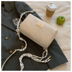 Close-up of cream cylinder bag featuring chic woven shoulder strap and golden logo tag