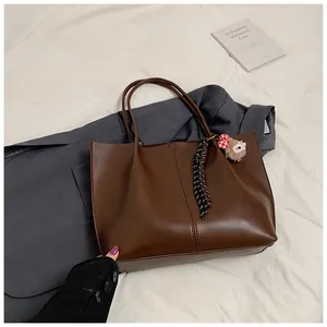 Detail of dark brown leather tote bag with sheep plush charm and woven rope decoration