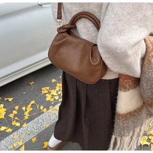 Détail du sac nuage plissé marron avec poignée ronde et garniture dorée sur feuilles d'automne
