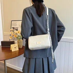 White minimalist crossbody bag with rope strap shown on model in a cozy interior