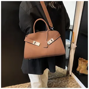 Brown leather tote bag featuring metal buckles and wide shoulder strap shown on model