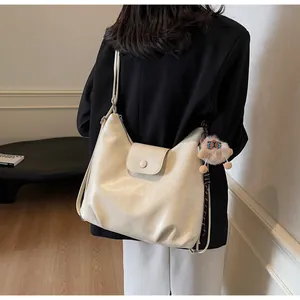 Dettaglio di una borsa tote in pelle bianco crema con ciondolo in peluche e finitura