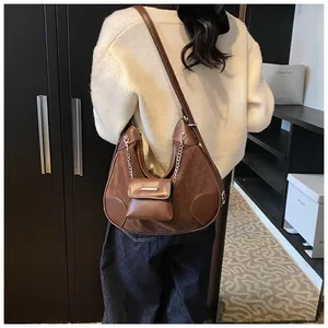 Detalle de bolso hobo marrón con mezcla de texturas y accesorio de cadena plateada