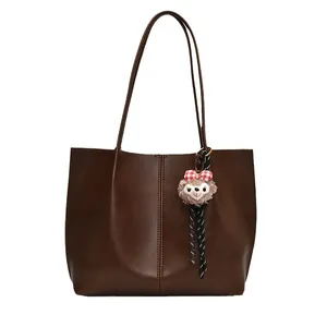 Brown leather tote bag with a plush bear charm on white background for women