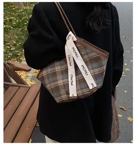 Detail of vintage plaid tote bag with leather trim and decorative ribbons on autumn street