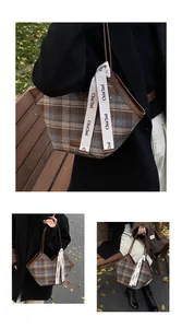 Detail of checkered fabric tote bag with leather trim and decorative lettered strap