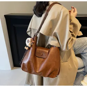 Borsa hobo vintage marrone in ecopelle abbinata a un trench kaki e un ciondolo di peluche