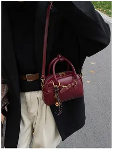 Detail of burgundy Boston bag with golden zipper and woven charm on a black coat