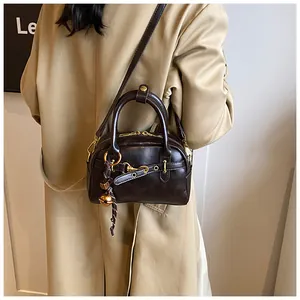 Detail of dark brown vintage Boston bag with gold hardware and bell charm on beige coat