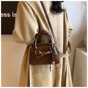 Detail of vintage brown leather bag with golden buckle and bell charm on a beige coat