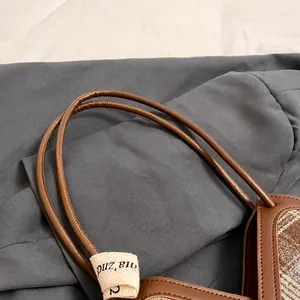 Detail of brown leather handles and classic plaid fabric stitching on tote bag