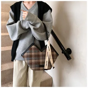 Detail of plaid tote bag with V-shaped opening and decorative logo strap on model