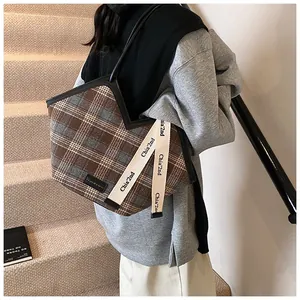 Detail of plaid fabric tote bag featuring black trim and wide printed shoulder strap