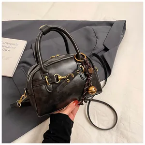 Macro detail of black vintage Boston bag with gold buckle and bell charm on a suit