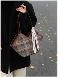 Detail of plaid tote bag with V-shaped leather trim and decorative ribbon in autumn setting