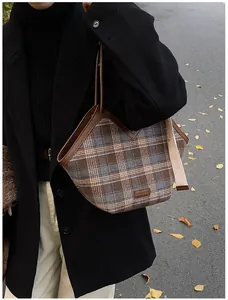 Detail of plaid tote bag with brown leather trim and scarf on autumn street