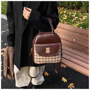 Detail of vintage brown leather backpack with plaid panels and bear patch on park bench