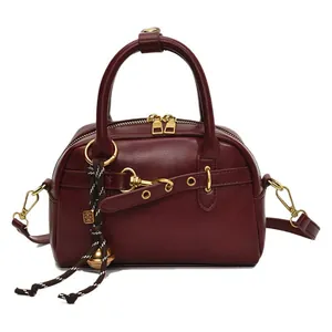 Deep red leather top-handle bag with gold hardware and woven charm on white background