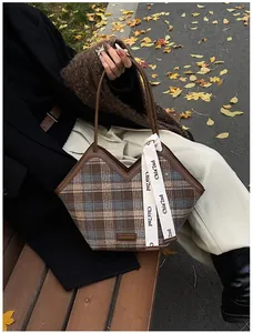Detail of plaid tote bag featuring leather handles and ribbon on wood bench with leaves