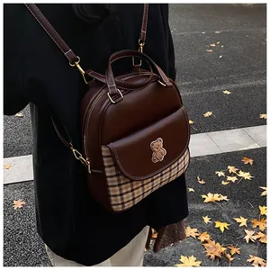 Detail of dark brown backpack featuring brown plaid pocket and a cute bear patch