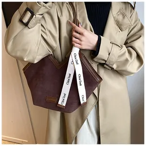 Close-up of dark brown suede tote bag featuring a V-cut top and white lettered webbing strap