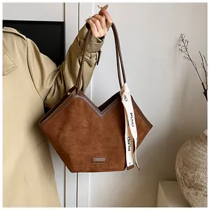Detail of a brown suede tote bag with silk scarf accessory and minimalist logo tag
