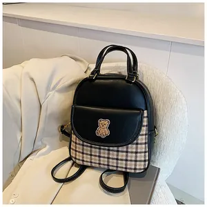 Detail of a vintage backpack featuring black leather, plaid fabric, and bear embroidery