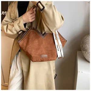 Detail of a brown suede tote bag with V-shaped opening and white ribbon ornament