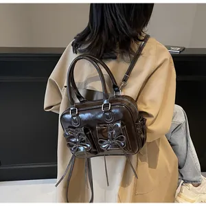 Detail of a dark brown glossy PU leather bag with bows worn over a trench coat