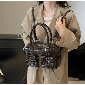 Detail of dark brown patent leather underarm bag featuring bow pockets and white stitching