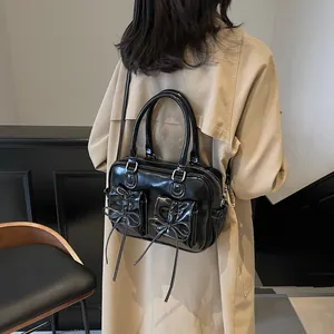 Elegant black shoulder bag with bow details and contrast stitching worn with a beige coat