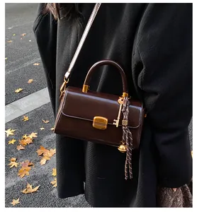 Detailed view of the dark brown leather shoulder bag with golden lock and tassel charm